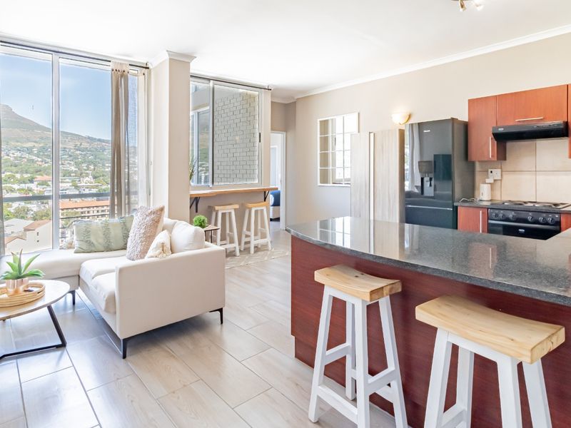 Modern open-plan living area featuring a well-appointed kitchen with granite countertops, breakfast bar, and floor-to-ceiling windows offering expansive city and mountain views.