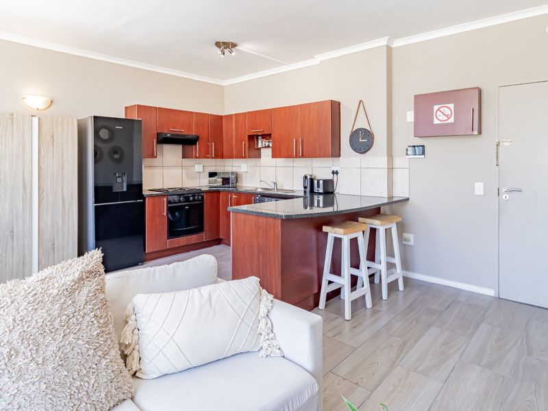 Open-plan kitchen featuring wood-finish cabinetry, granite countertops, and integrated appliances, seamlessly flowing into the living area with modern laminate flooring.