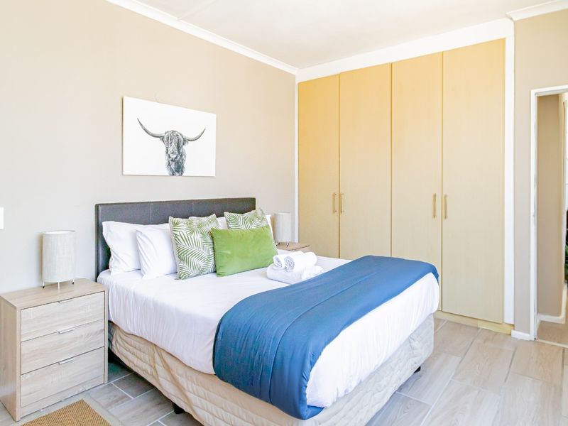 A well-maintained bedroom featuring neutral walls, tiled flooring, and ample built-in cupboard storage, with direct access to an en-suite bathroom.