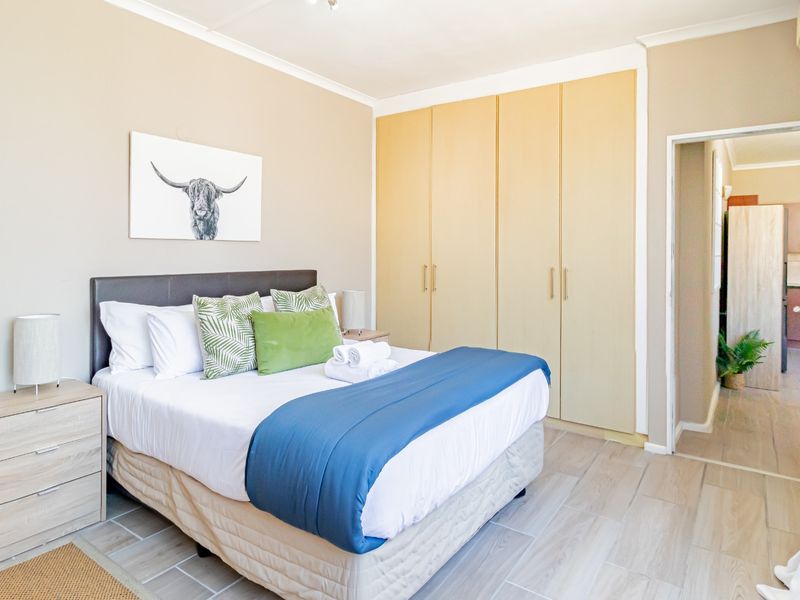 A well-lit bedroom featuring neutral walls, tiled flooring, and ample built-in cupboard storage, with an integrated air conditioning unit.