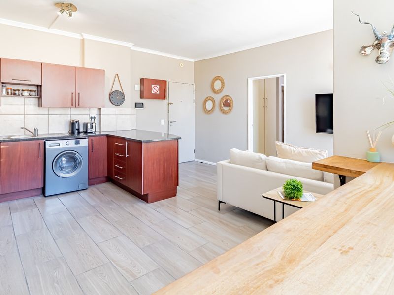 Open-plan living area featuring a functional kitchen with wood-finish cabinetry, integrated laundry appliance, and modern wood-look floor tiles throughout the space.