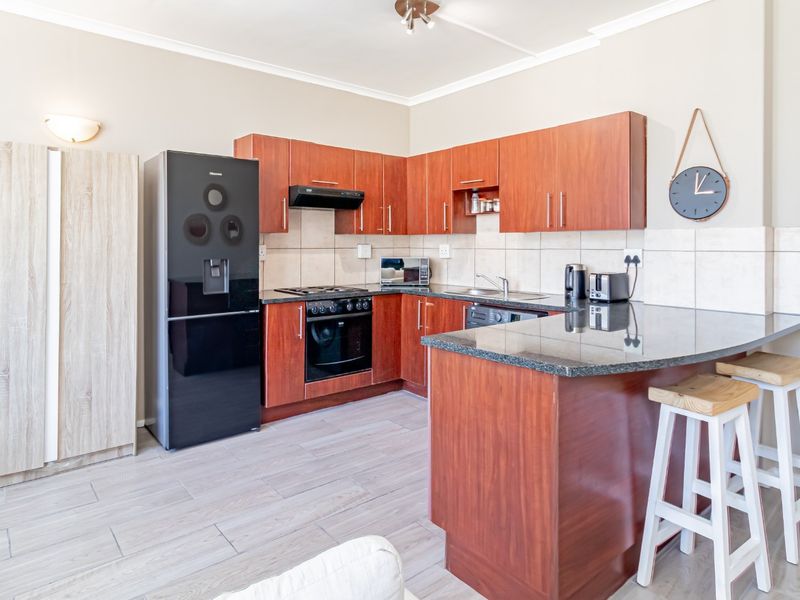 A functional kitchen featuring wood-finish cabinetry, granite countertops, a breakfast bar, and integrated appliances, set against a neutral tiled backsplash.