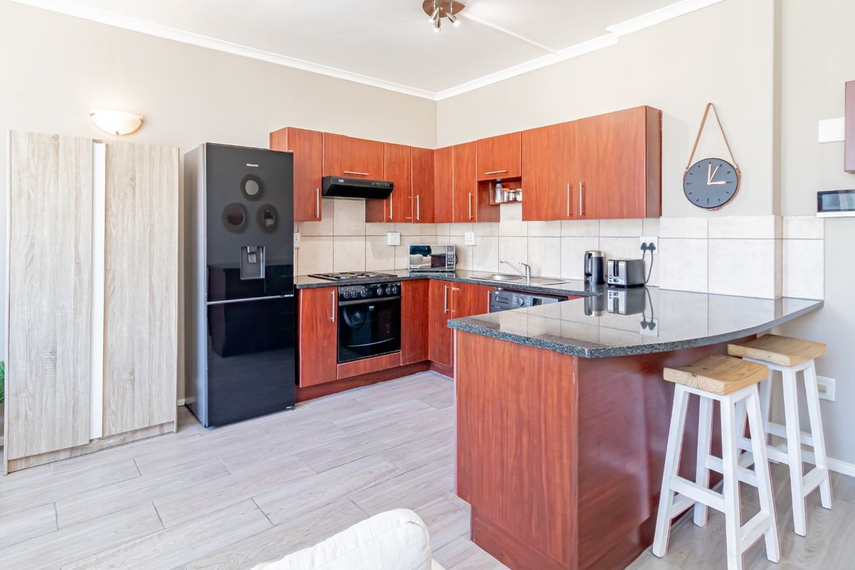 A functional kitchen featuring wood-finish cabinetry, granite countertops, a breakfast bar, and integrated appliances, set against a neutral tiled backsplash.