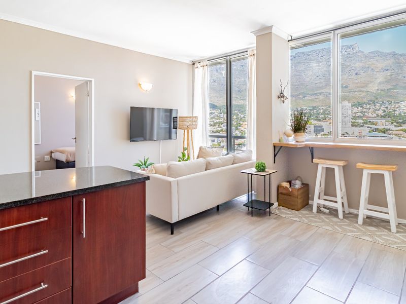 Bright open-plan living area featuring a modern kitchen with granite countertops, tiled floors, and large windows offering expansive mountain and city views.