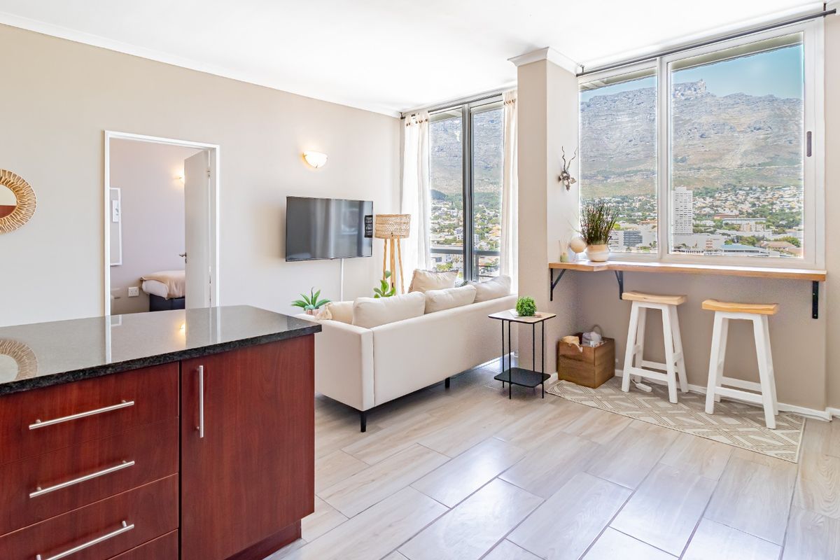 Bright open-plan living area featuring a modern kitchen with granite countertops, tiled floors, and large windows offering expansive mountain and city views.