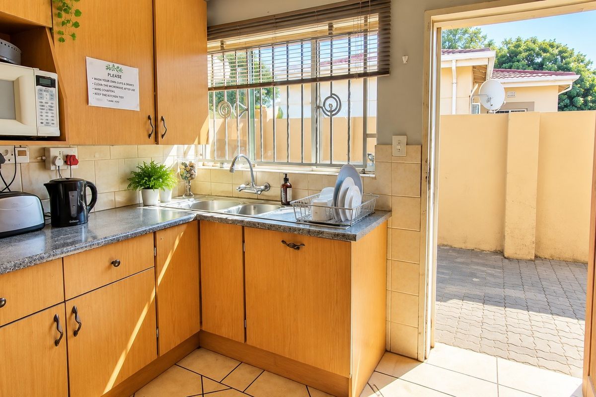 A functional kitchen featuring laminate cabinetry, tiled backsplash, and a double basin sink, with direct access to an outdoor paved area.