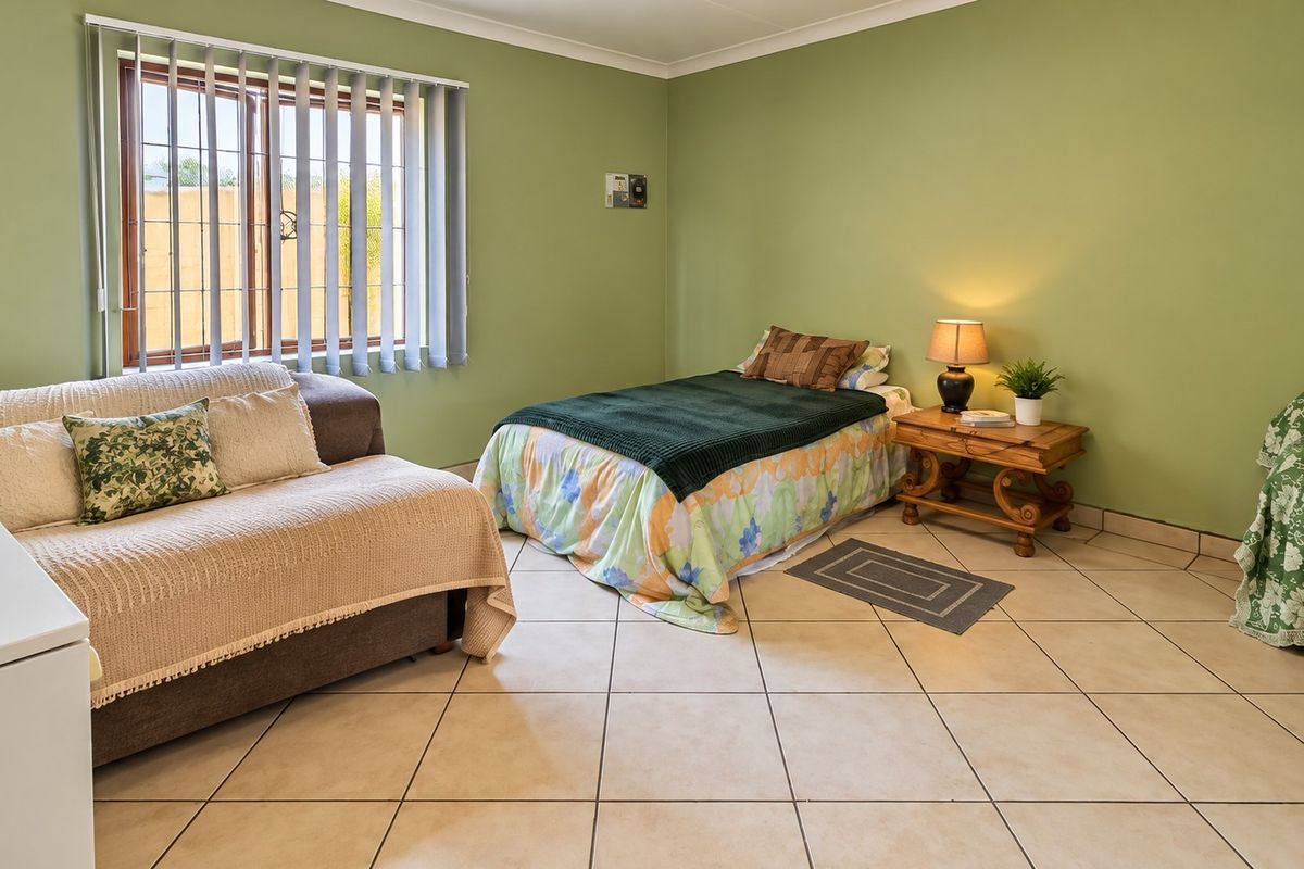 A functional bedroom featuring tiled flooring, vertical blinds, and security bars on the window, providing a simple and practical living space.