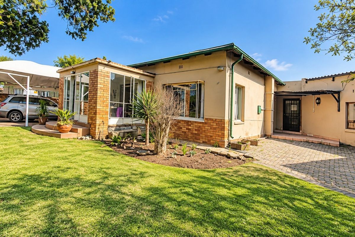 Rear view of the property featuring a brick facade, paved driveway, carport, and a well-maintained garden area.