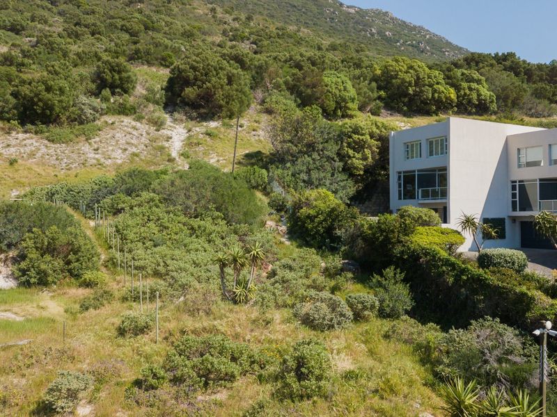 Aerial view of a residential property situated on a sloped, vegetated hillside, showcasing the integration of the building with the natural landscape.
