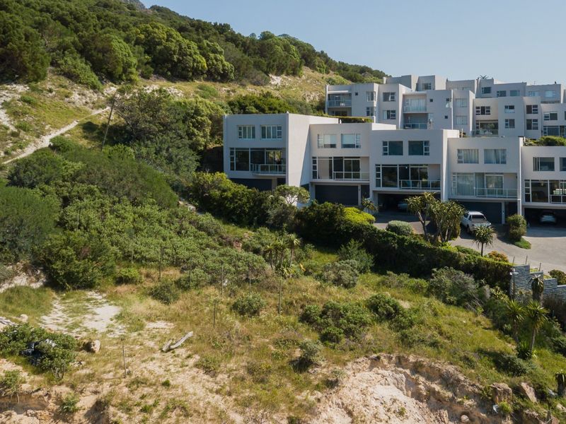 An aerial view of a sloped residential vacant land plot adjacent to an established apartment complex, featuring natural vegetation and hillside terrain.