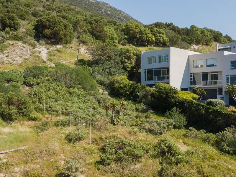 Aerial view of a sloped residential plot featuring natural vegetation, adjacent to an existing multi-story residential building.