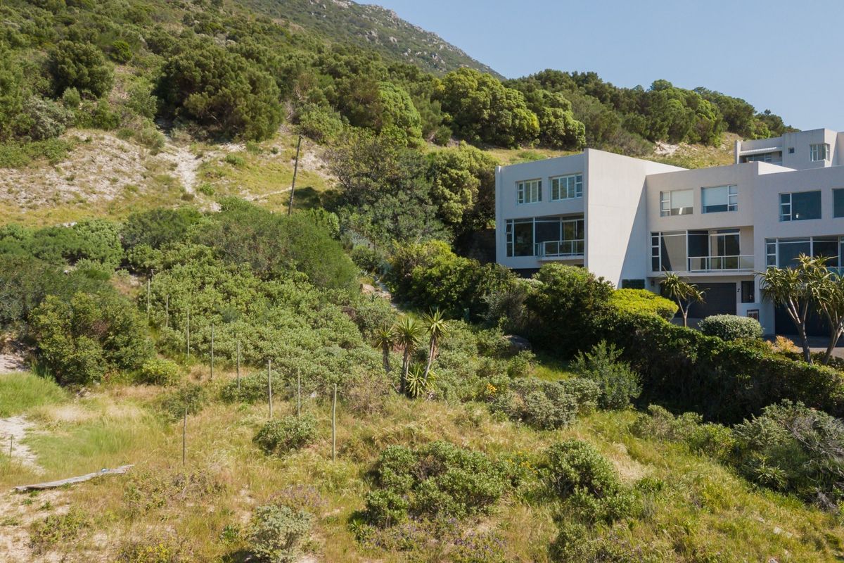 Aerial view of a sloped residential plot featuring natural vegetation, adjacent to an existing multi-story residential building.