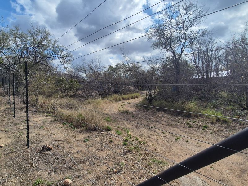 A view of a vacant residential plot featuring natural vegetation, a dirt access track, and perimeter electric fencing.