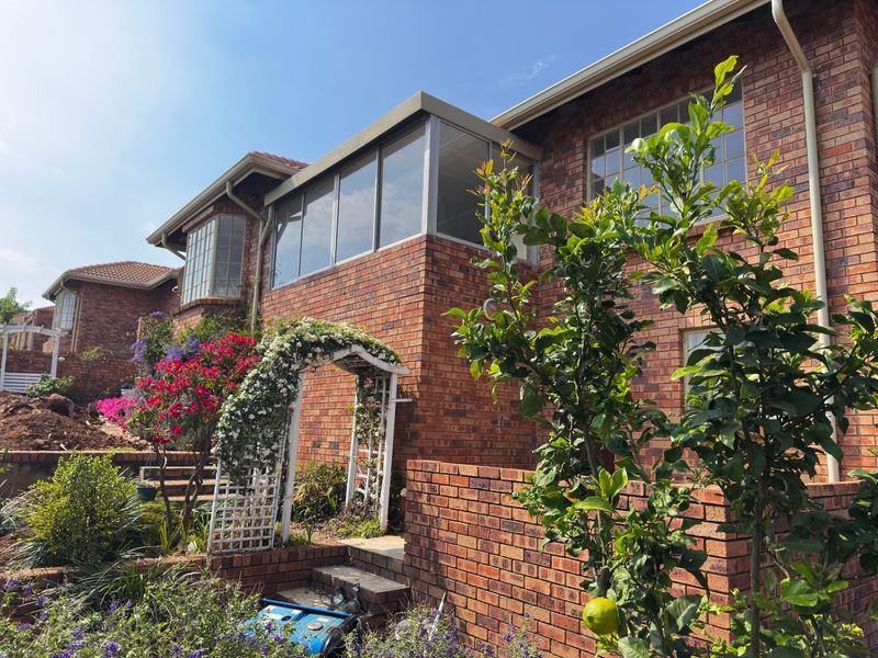 Rear view of a face brick townhouse featuring an enclosed upper-level balcony, established garden, and brick retaining walls.