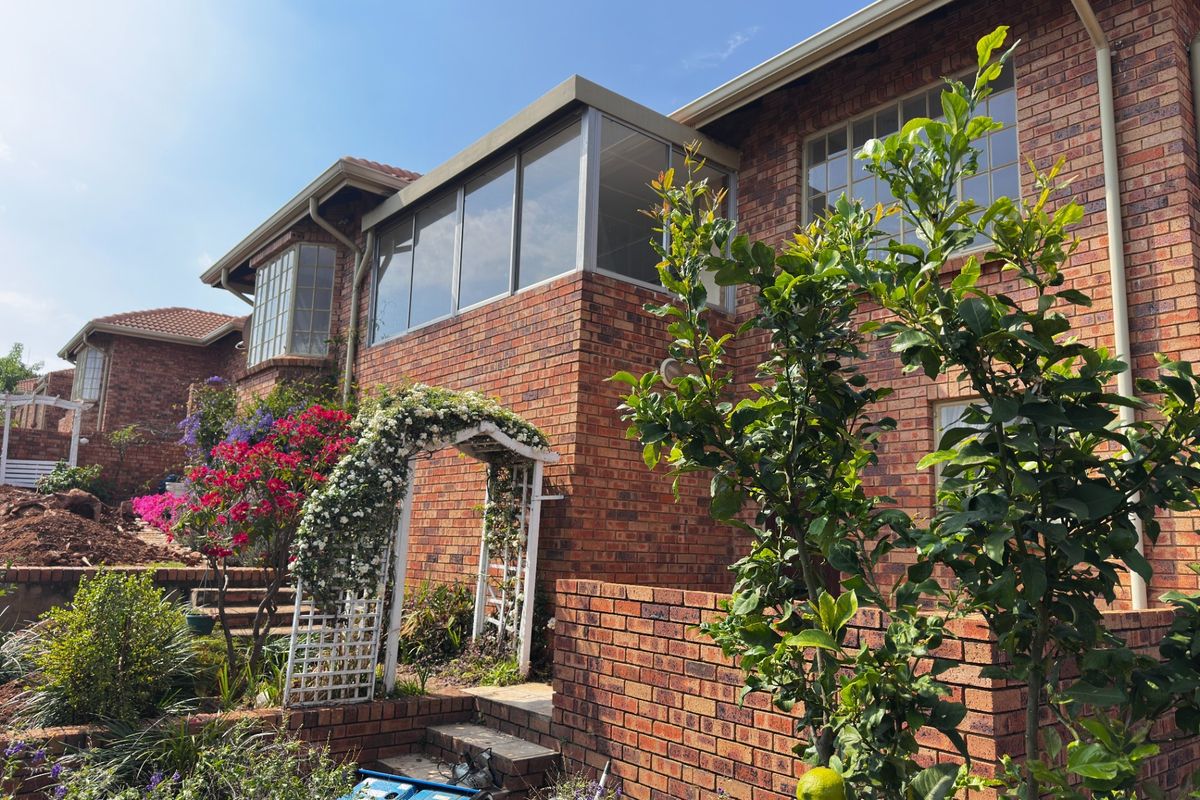 Rear view of a face brick townhouse featuring an enclosed upper-level balcony, established garden, and brick retaining walls.