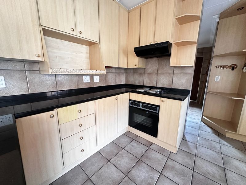 A functional kitchen featuring light wood-tone cabinetry, black granite countertops, built-in oven, and tiled flooring throughout.
