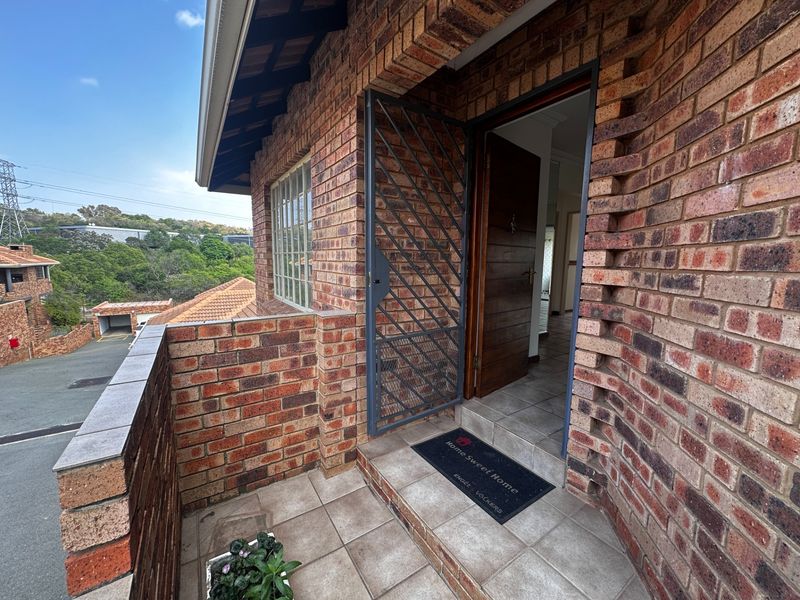 A welcoming townhouse entrance featuring a face brick facade, secure metal gate, and tiled porch area leading into the main living space.