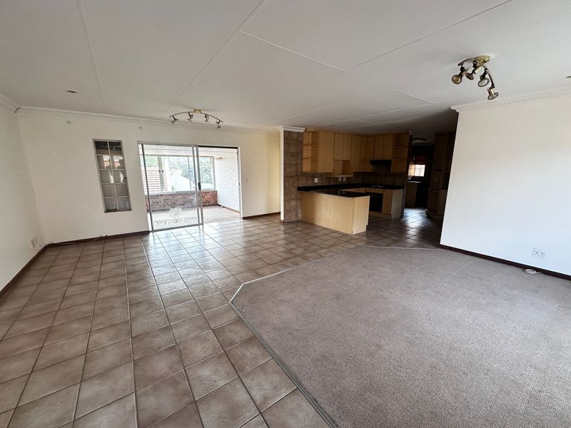 Spacious open-plan living and kitchen area featuring tiled and carpeted flooring, built-in cabinetry with granite countertops, and access to an enclosed patio.