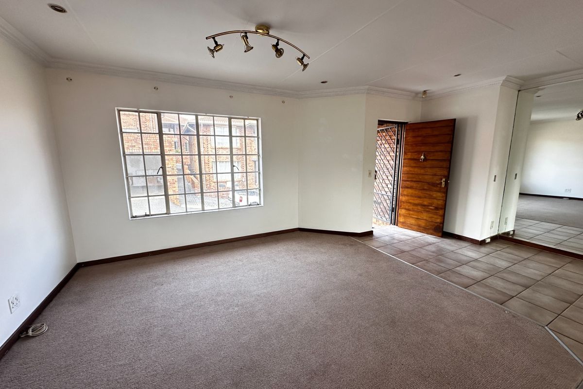 Spacious, empty living area featuring neutral carpeting, a tiled entrance section, and a large mirrored built-in cupboard, offering a blank canvas for personalization.