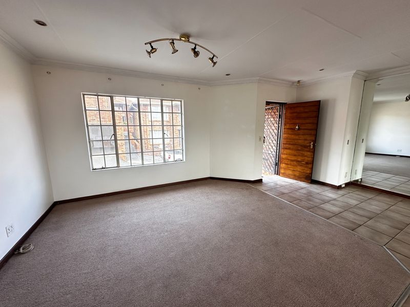 Spacious, empty living area featuring neutral carpeting, a tiled entrance section, and a large mirrored built-in cupboard, offering a blank canvas for personalization.