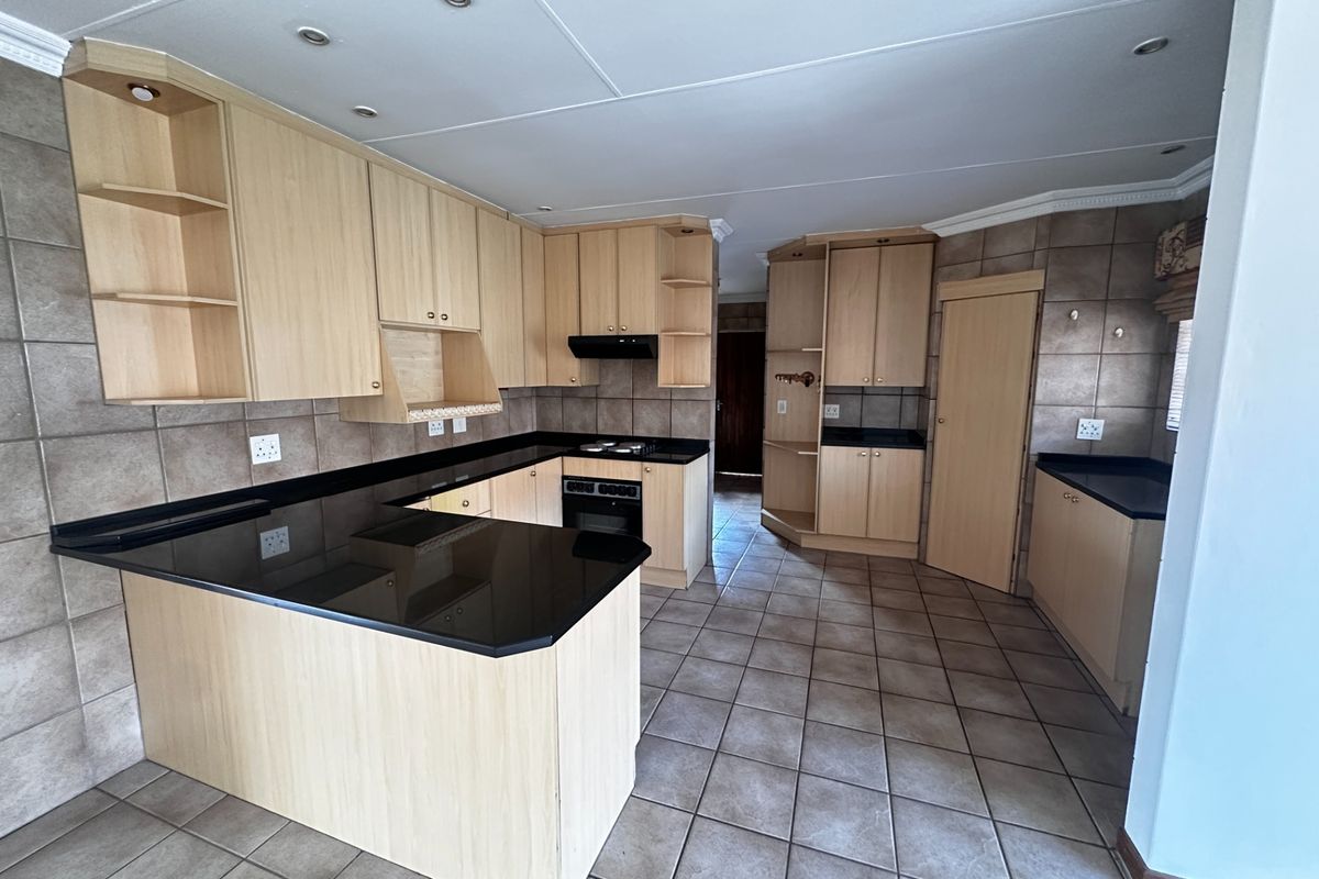 Spacious kitchen featuring light wood cabinetry, black granite countertops, built-in oven and hob, and neutral tiled flooring throughout.