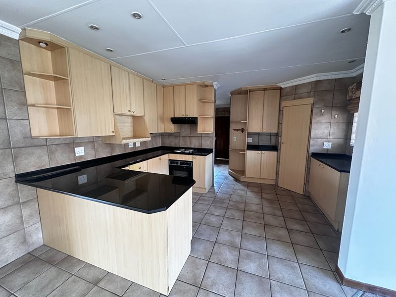 Spacious kitchen featuring light wood cabinetry, black granite countertops, built-in oven and hob, and neutral tiled flooring throughout.