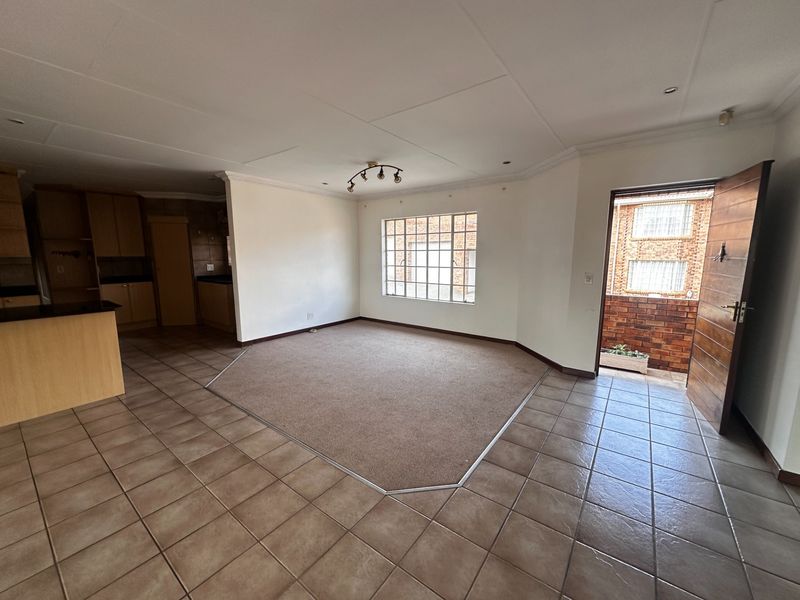 Spacious open-plan living area featuring tiled floors, a central carpeted section, and an adjoining kitchen with built-in cabinetry and direct outdoor access.