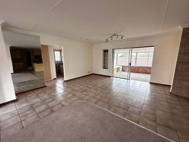 Spacious open-plan living area featuring tiled and carpeted flooring, a large mirrored wall, and sliding glass doors leading to an enclosed patio.