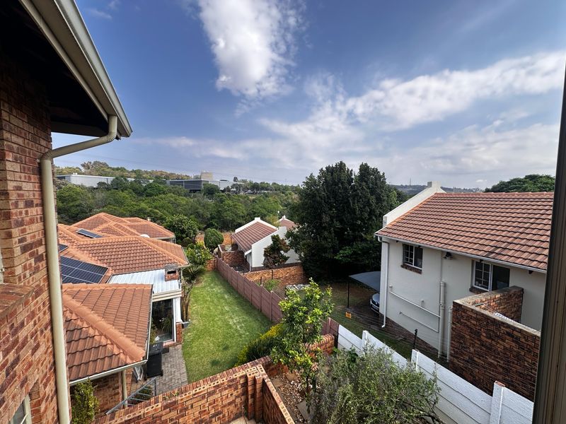 Elevated view overlooking the townhouse complex, featuring tiled roofs, solar panels, and established garden areas with brick and concrete boundary walls.