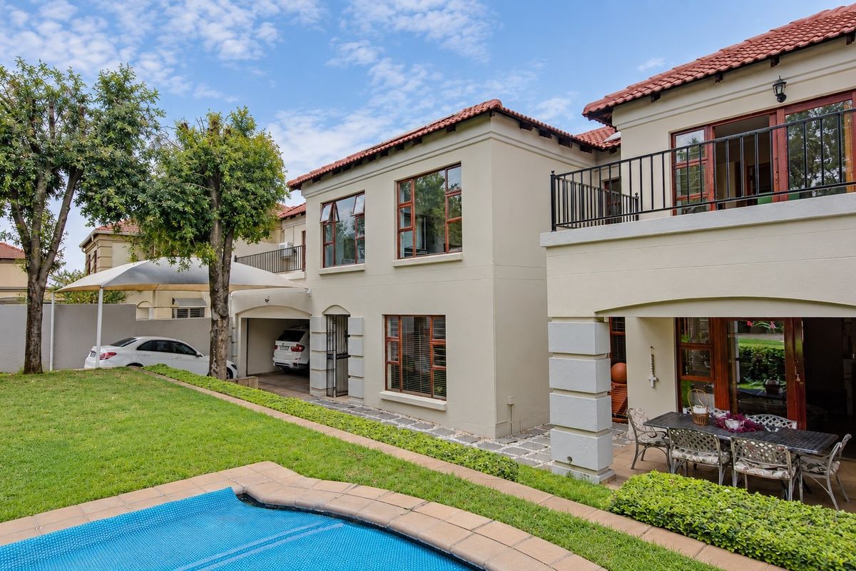 Rear view of a two-story residence featuring a swimming pool, covered patio, upper-level balcony, and integrated carport area.