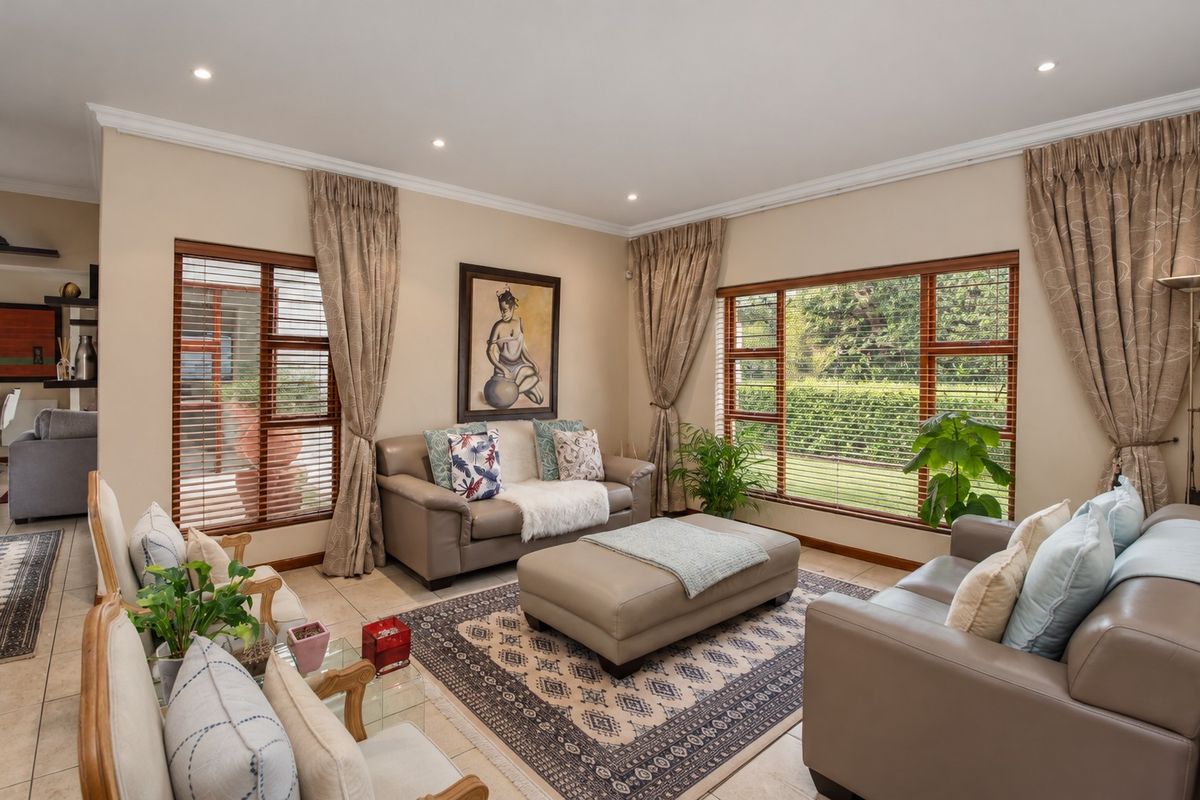 A well-maintained living room featuring tiled floors, recessed downlighting, and large timber-framed windows with venetian blinds overlooking the garden.