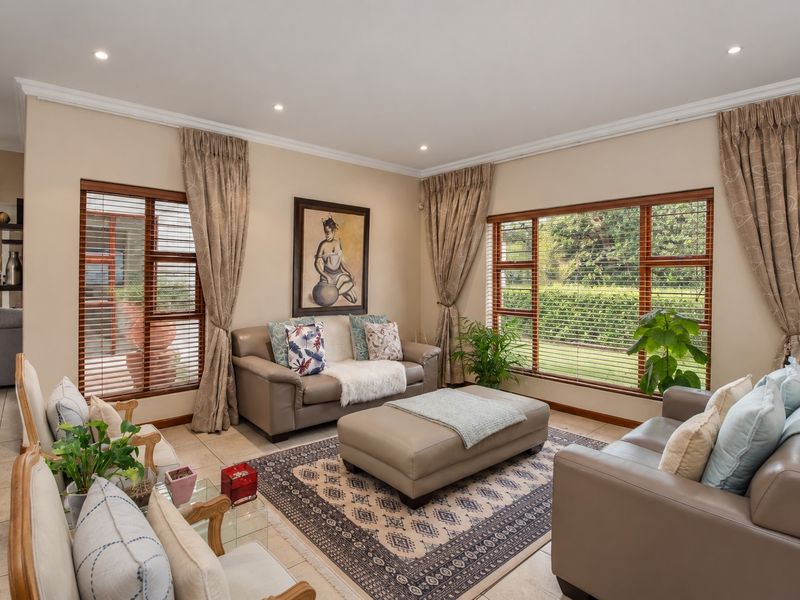 A well-maintained living room featuring tiled floors, recessed downlighting, and large timber-framed windows with venetian blinds overlooking the garden.