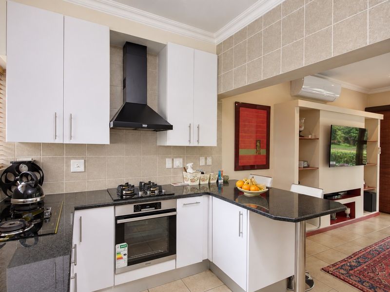 Modern kitchen featuring white cabinetry, granite countertops, built-in oven, gas hob, and a breakfast bar, seamlessly flowing into the adjacent living area.