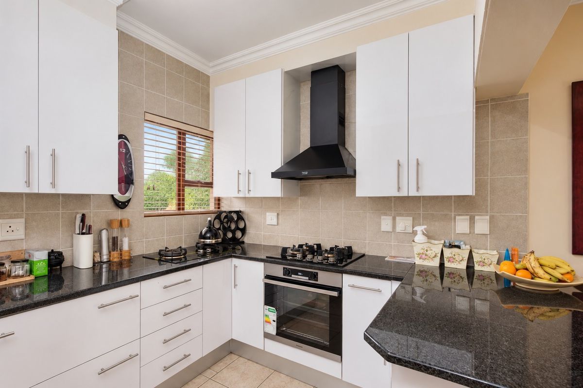 Modern kitchen featuring granite countertops, white cabinetry, built-in oven, gas hob, and a tiled backsplash.
