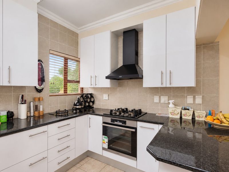 Modern kitchen featuring granite countertops, white cabinetry, built-in oven, gas hob, and a tiled backsplash.