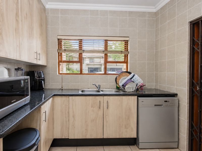 A functional scullery featuring light wood-look cabinetry, dark granite countertops, a double basin sink, and tiled walls with a security gate.