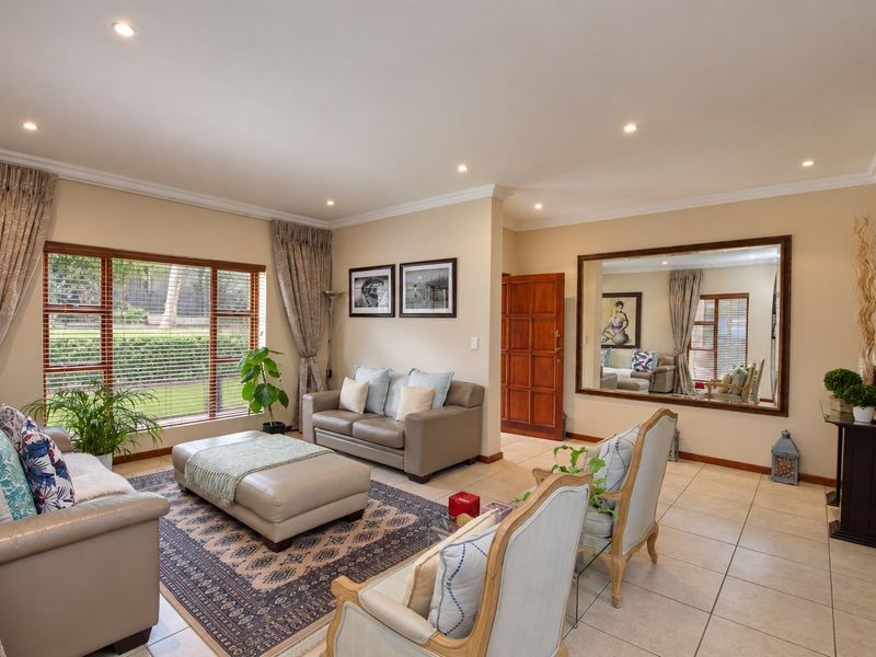 A well-maintained living room featuring tiled floors, recessed downlights, a large wall mirror, and a stone feature wall with natural light.