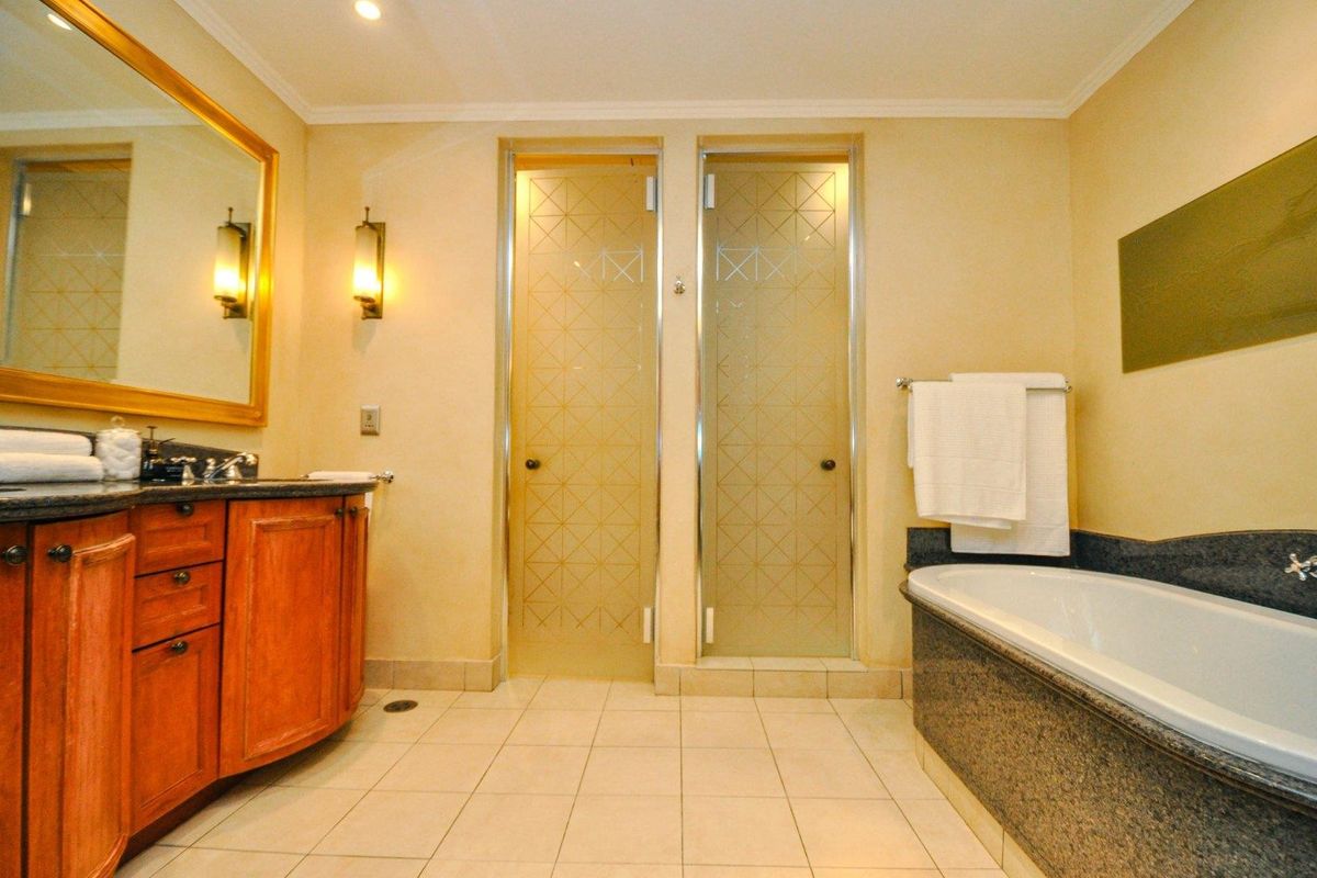 A well-appointed bathroom featuring a wooden vanity with granite countertop, a built-in bathtub, and dual frosted glass doors leading to separate facilities.