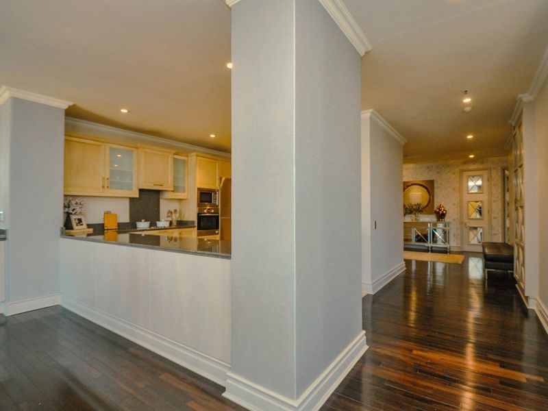 Open-plan kitchen area featuring granite countertops, built-in appliances, and elegant hardwood flooring, seamlessly flowing into the hallway and living space.