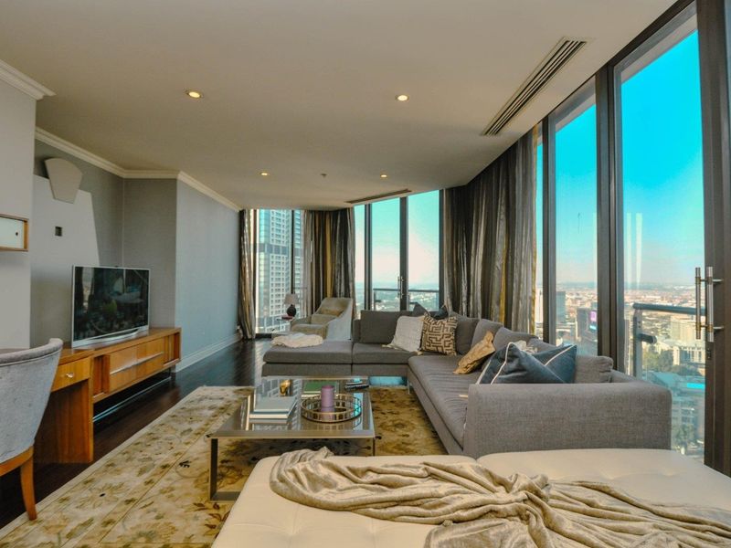 Spacious living room featuring floor-to-ceiling windows with expansive city views, recessed lighting, ducted air conditioning, and dark hardwood flooring.