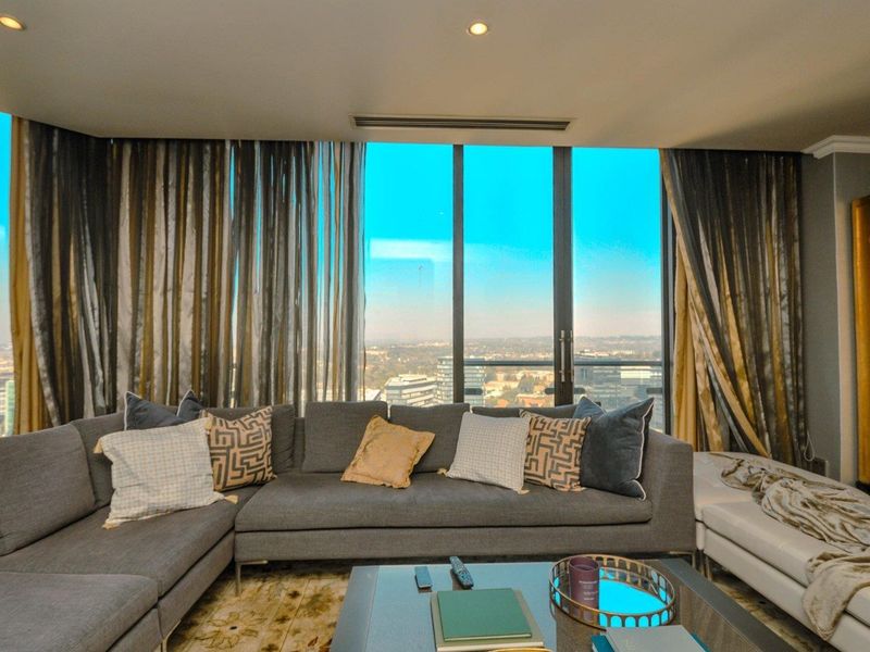 A modern living room featuring expansive floor-to-ceiling windows with panoramic city views, recessed lighting, and integrated ducted air conditioning.