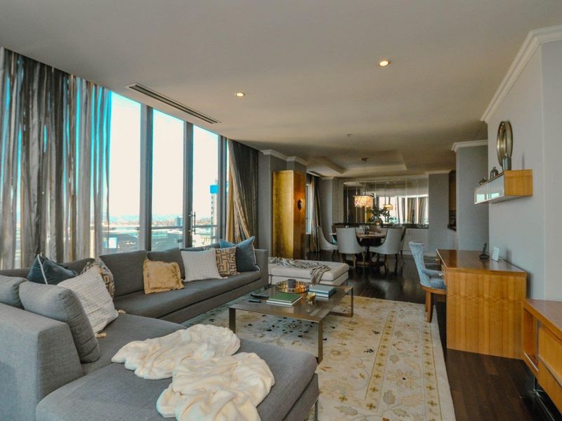 Spacious open-plan living and dining area featuring floor-to-ceiling windows, hardwood flooring, and modern recessed lighting with a sophisticated mirrored wall detail.