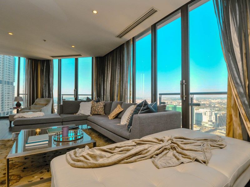 Modern living room featuring floor-to-ceiling windows with expansive city views, ducted air conditioning, and recessed lighting in a high-rise apartment setting.