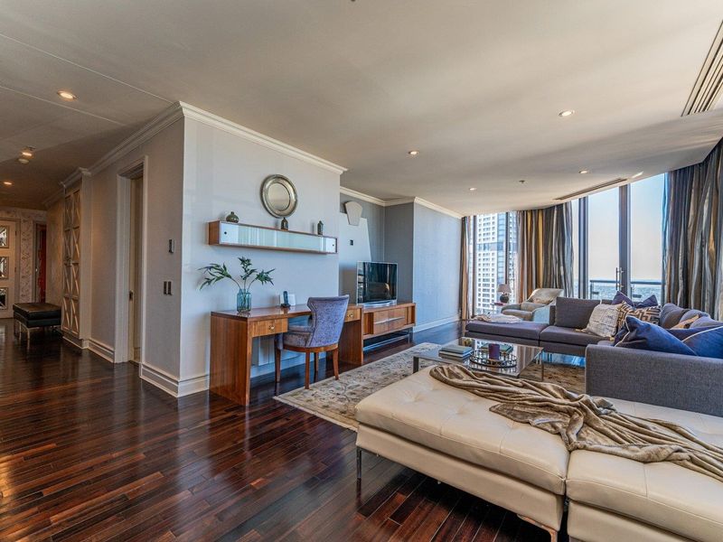Spacious living room featuring rich hardwood flooring, recessed lighting, and expansive floor-to-ceiling windows offering natural light and city views.