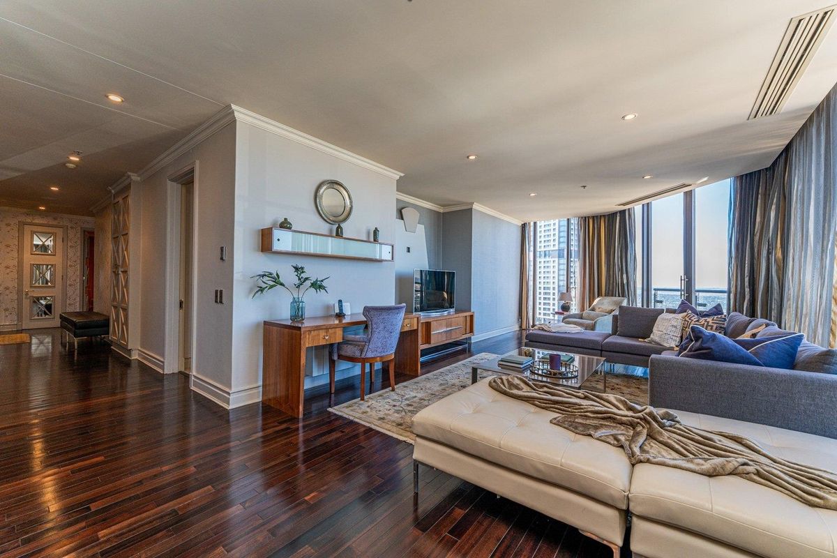 Spacious living room featuring rich hardwood flooring, recessed lighting, and expansive floor-to-ceiling windows offering natural light and city views.