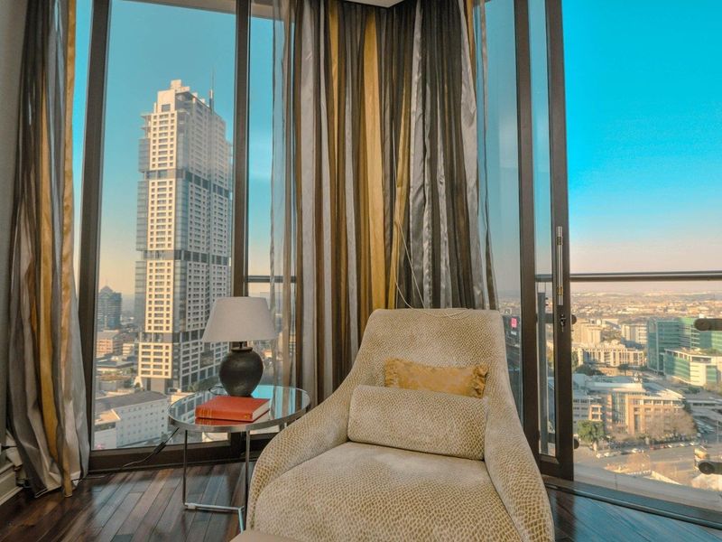 A bright living space featuring floor-to-ceiling windows and a sliding glass door, offering expansive urban views and access to a balcony.