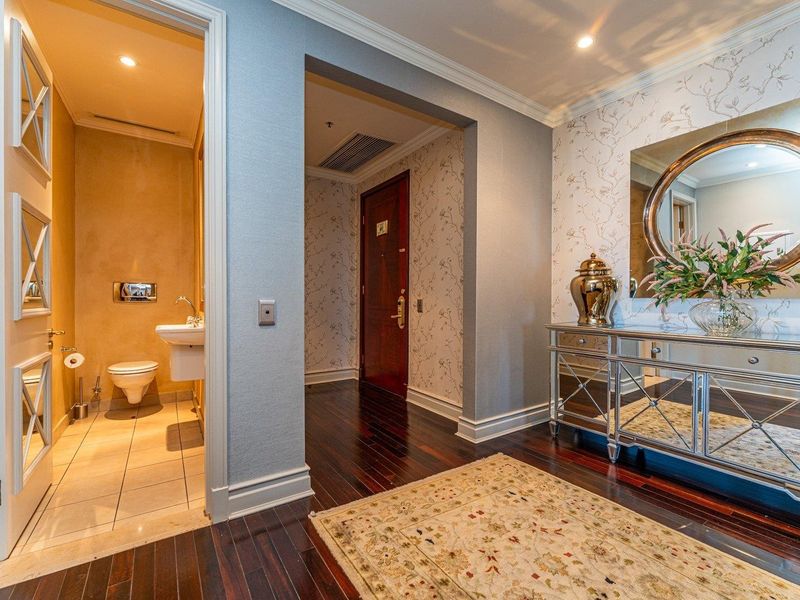 Elegant entrance foyer featuring dark hardwood flooring, decorative wallpaper, crown molding, and access to a compact guest bathroom with modern fixtures.