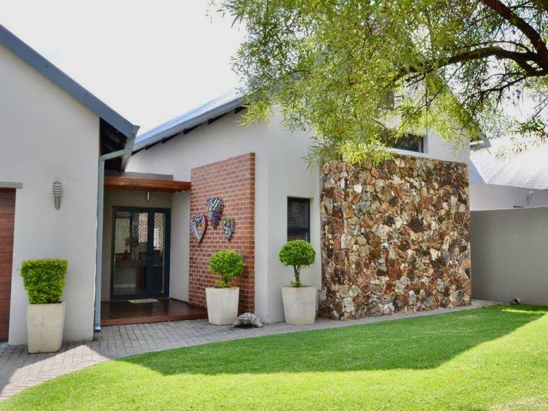 Front elevation of a modern house featuring a combination of stone cladding, brick accents, a paved driveway, and a timber entrance deck.