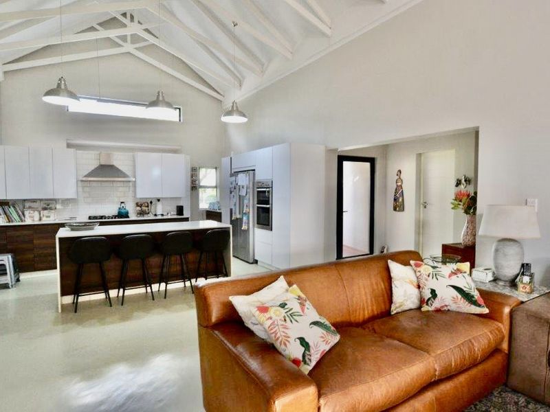 Spacious open-plan living area featuring a modern kitchen with island, vaulted ceilings with exposed rafters, and polished concrete floors.