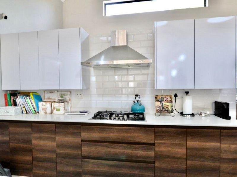 Modern kitchen featuring high-gloss white upper cabinets, wood-grain lower cabinetry, stone countertops, a gas hob, and a stylish subway tile backsplash.